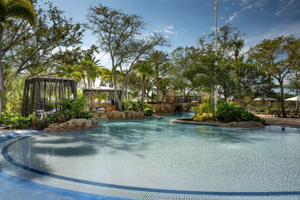 Resort swimming pool surrounded by palm trees, caged entertainment pavilions, and manicured landscaping