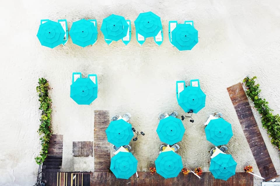 Aerial view of white sand beach with bright turquoise umbrellas and lounge chairs arranged in rows