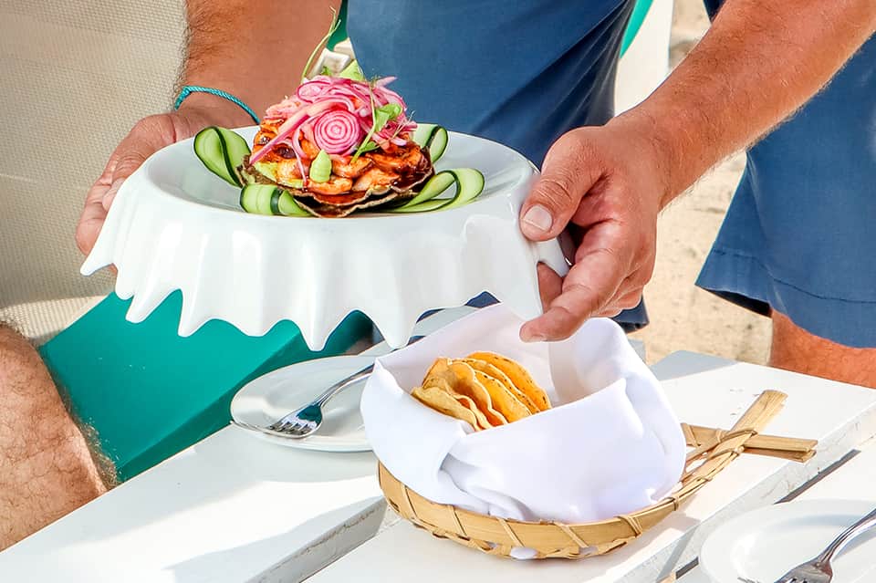 Server presenting decorative plate with fresh crab cake and cucumber garnish
