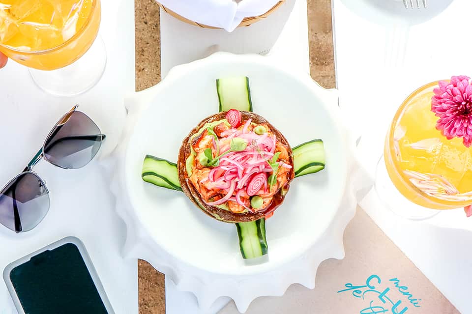 Overhead shot of gourmet salad plate with yellow drinks and sunglasses on cork surface