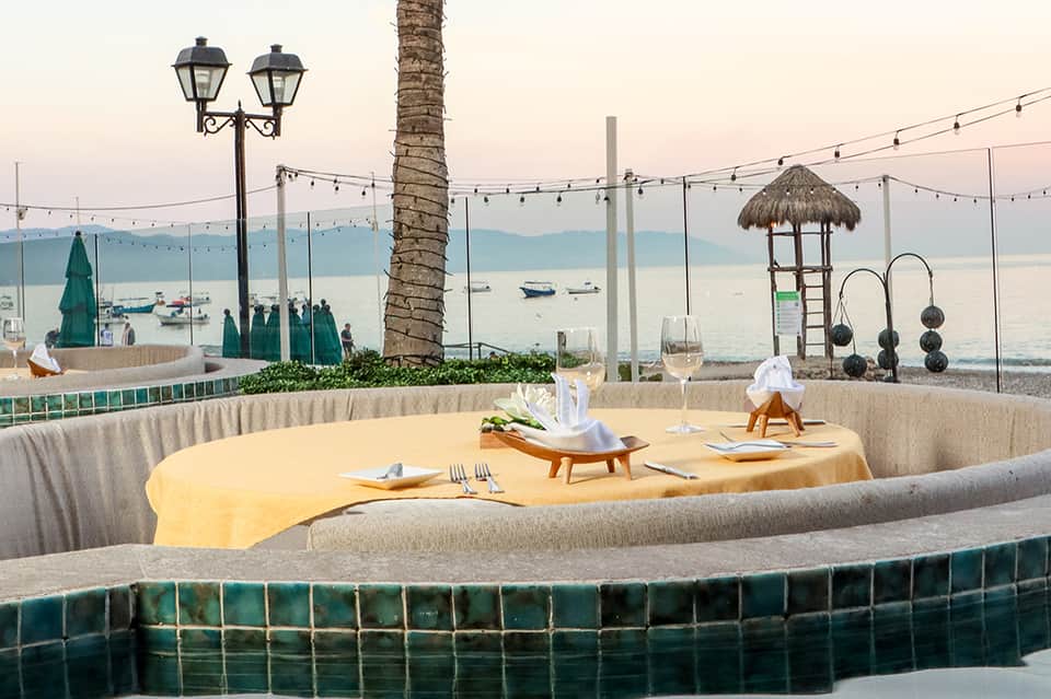 Oceanfront dining setup with yellow tablecloth, palm tree, and sea view beyond glass railing