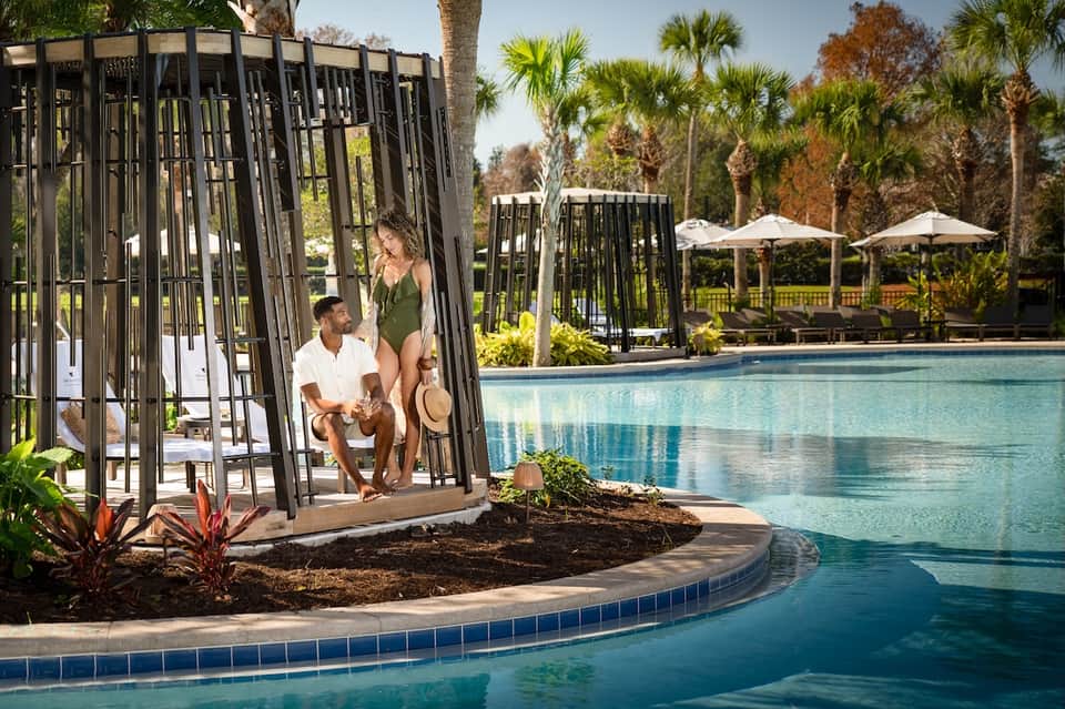 Luxury resort pool area with modern gazebo, palm trees, lounge chairs, and beach view