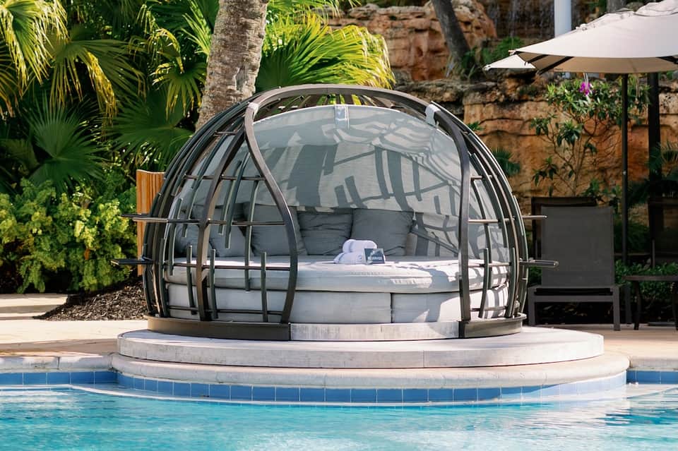 Modern spherical pod bed suspended over resort swimming pool surrounded by tropical landscaping