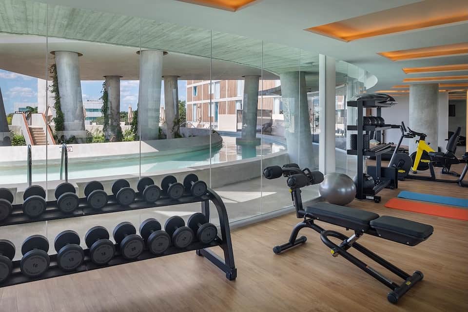 Modern fitness center with dumbbells, exercise bikes, and views of pool through glass walls