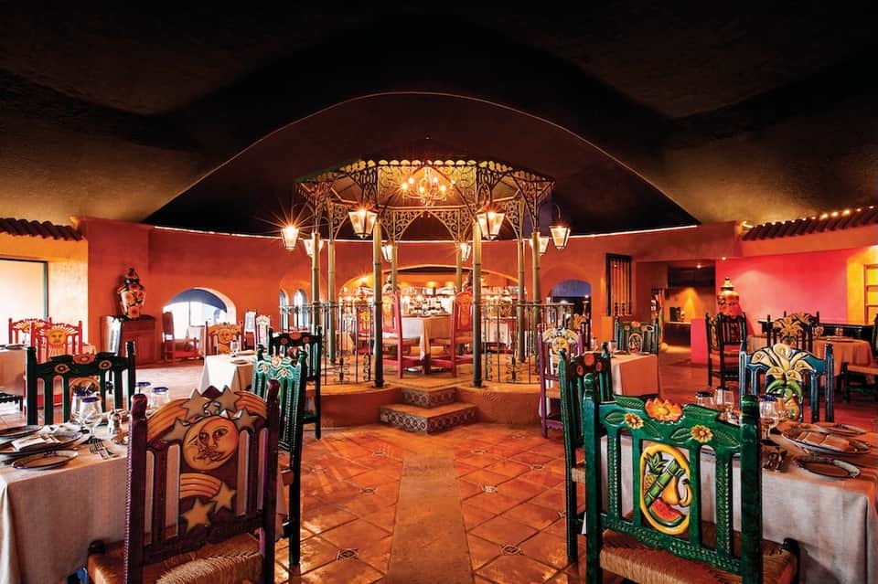Ornate Moroccan-style dining room with red walls, decorative chairs, and central brass chandelier