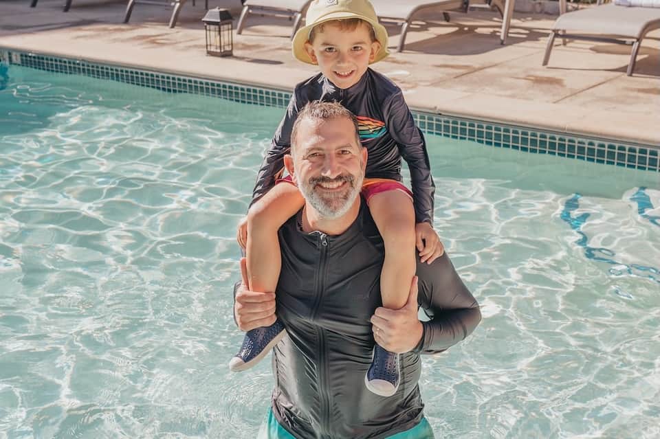 Father and young son enjoying pool time together in shallow resort water with sunny weather