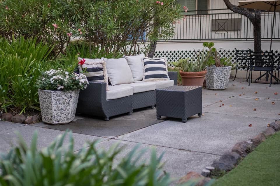 Dark wicker outdoor sofa with cushions and striped pillows surrounded by potted flowers