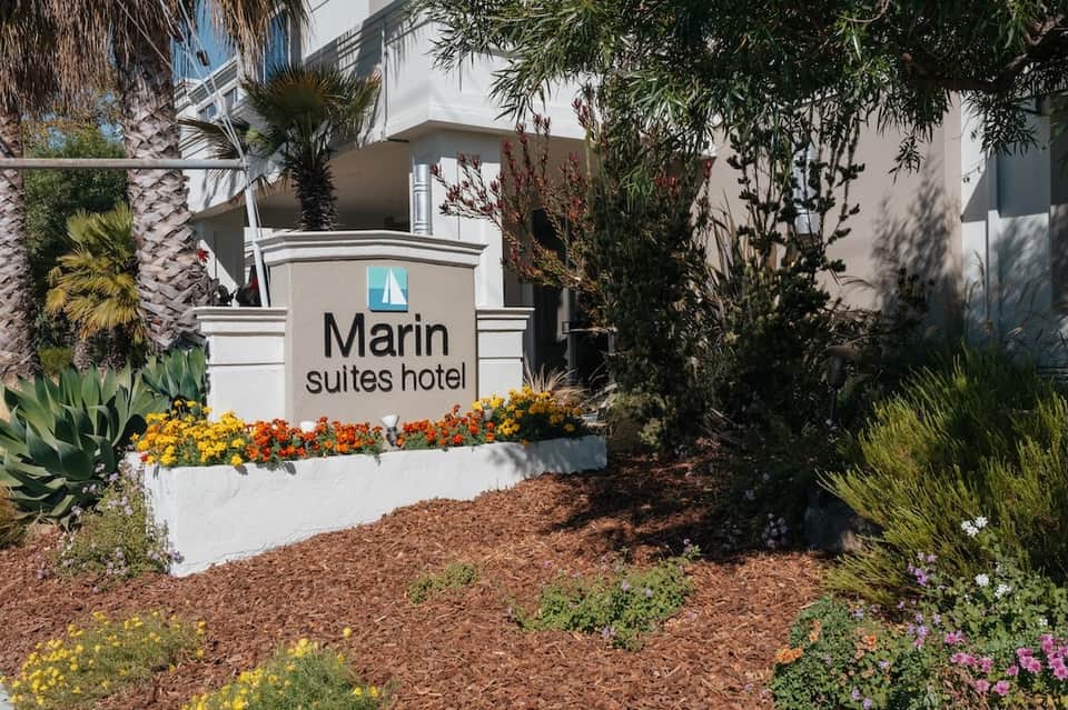 Marin Suites Hotel entrance sign with white stone base, surrounded by colorful flowers and desert plants
