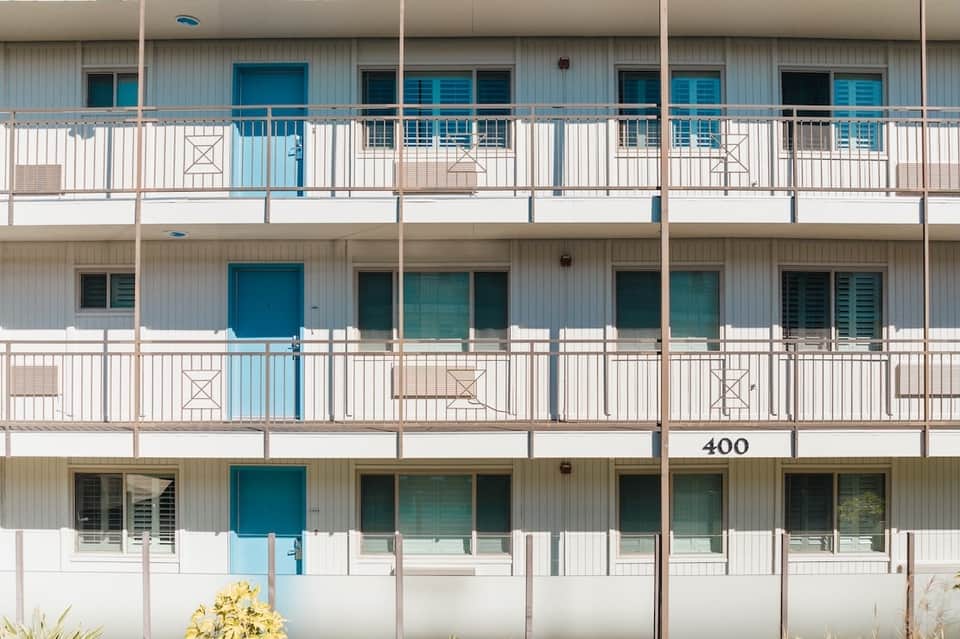 Three-story beachfront building exterior with white and blue railings and multiple balconies