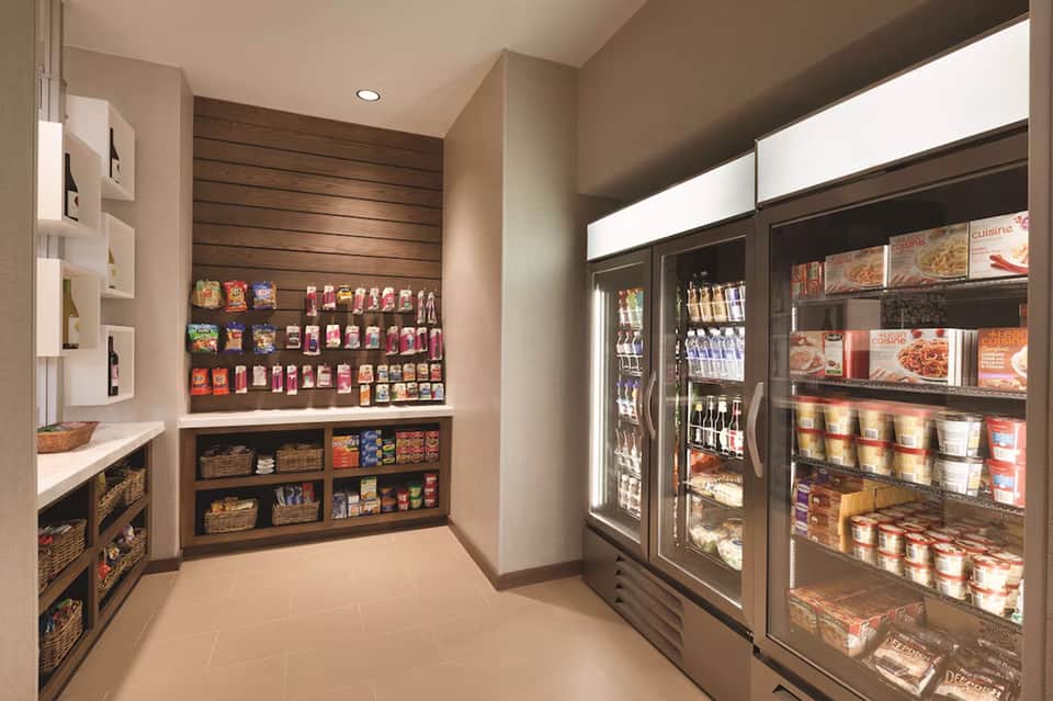 Hotel market convenience store with stocked shelves, refrigerated cases, and packaged snacks