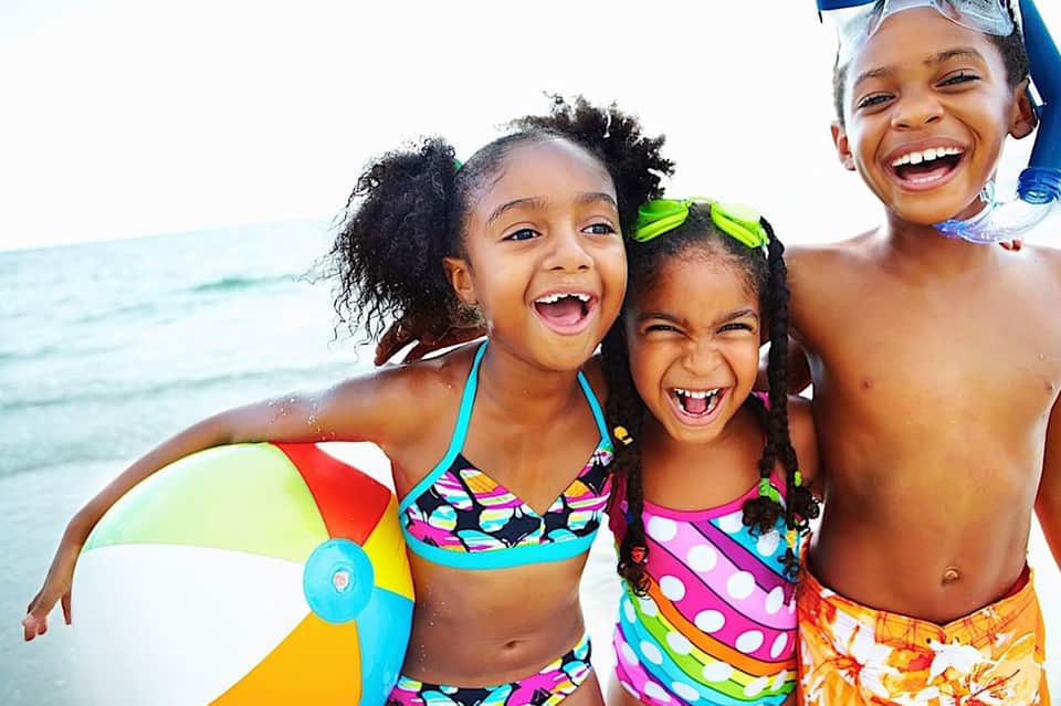 Children playing on beach wearing colorful swimwear and holding inflatable beach ball