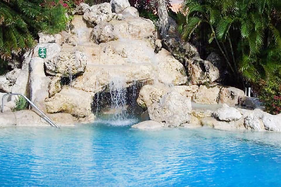 Resort swimming pool with turquoise water and natural rock waterfall surrounded by tropical vegetation