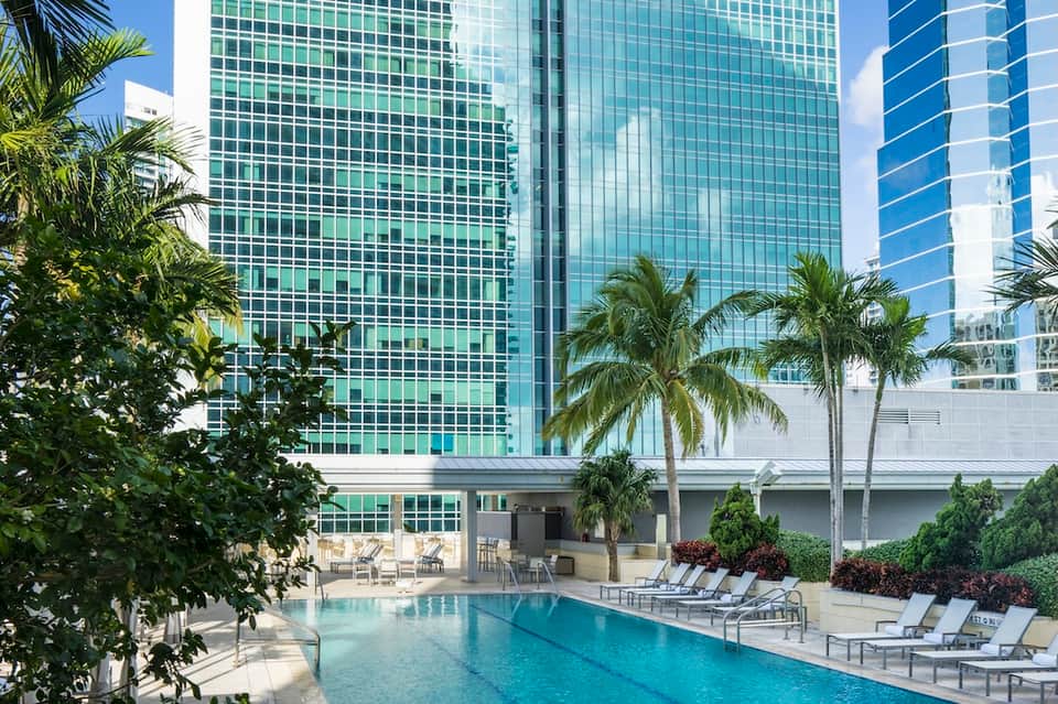 Resort pool surrounded by palm trees with modern glass high-rise hotel building in background
