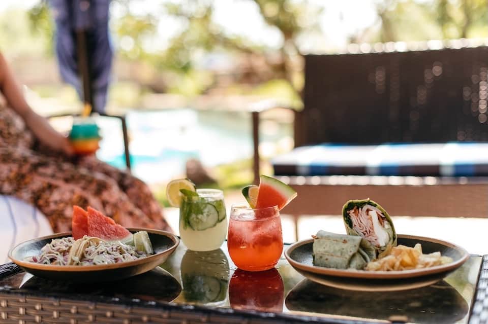 Poolside dining table with fresh wraps, watermelon, and colorful tropical cocktails