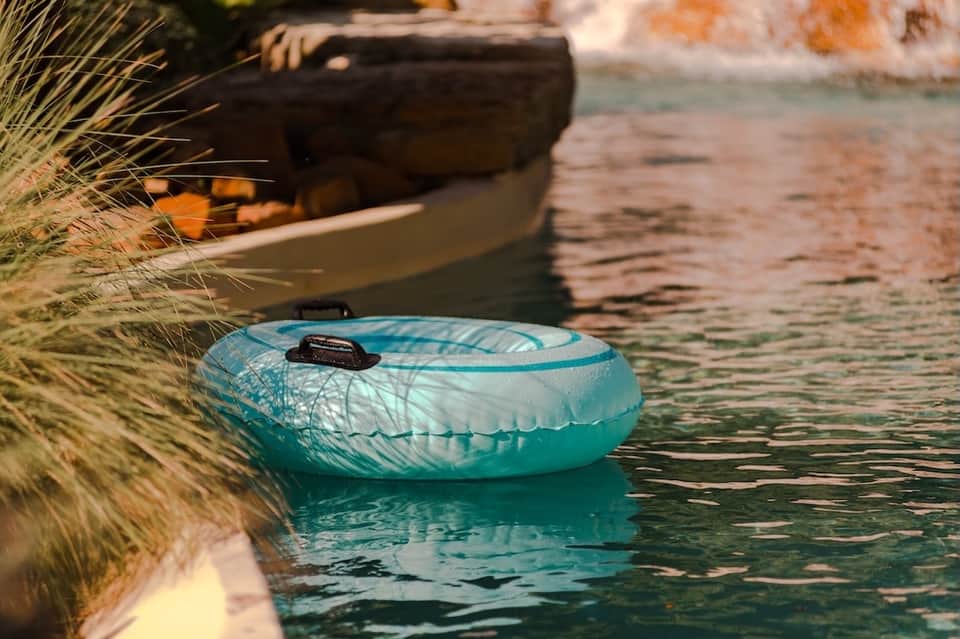 Turquoise inflatable float on calm waterway with wooden boat and coastal landscape in soft focus background