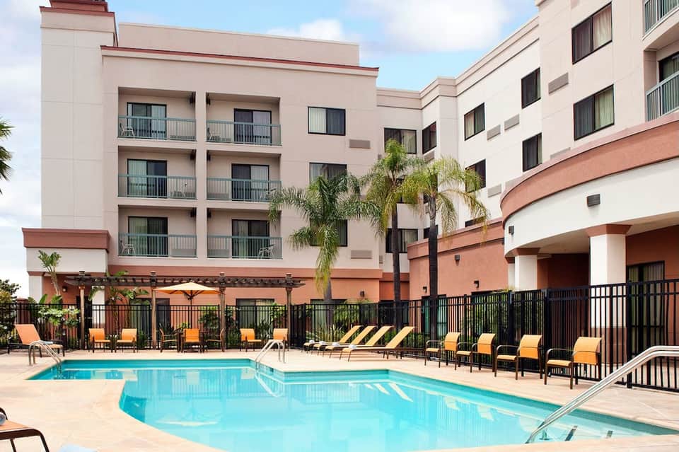 Hotel exterior courtyard with pool, lounge chairs, orange umbrellas, and multi-story building