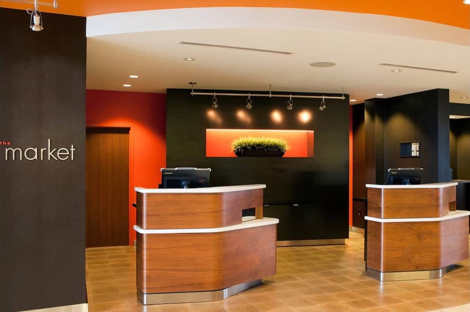 Modern hotel lobby reception area with orange and black accent walls, wooden curved desks, and ambient lighting