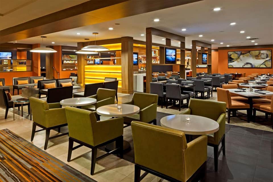 Contemporary restaurant interior with olive seating, orange accent walls, and modern pendant lighting