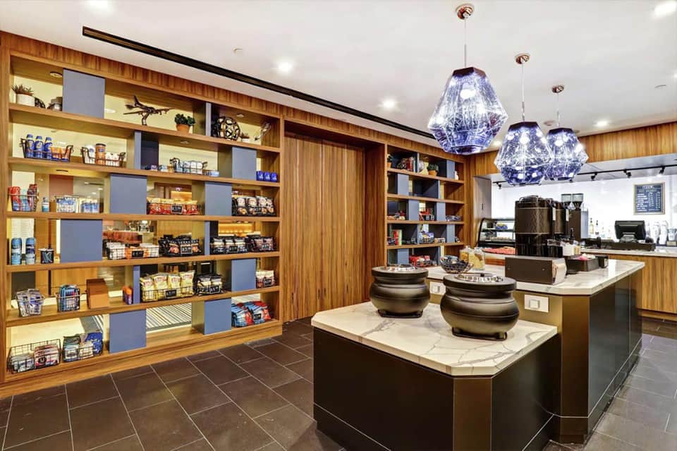 Modern resort café with wooden shelving displaying merchandise, pendant lighting, and service counter