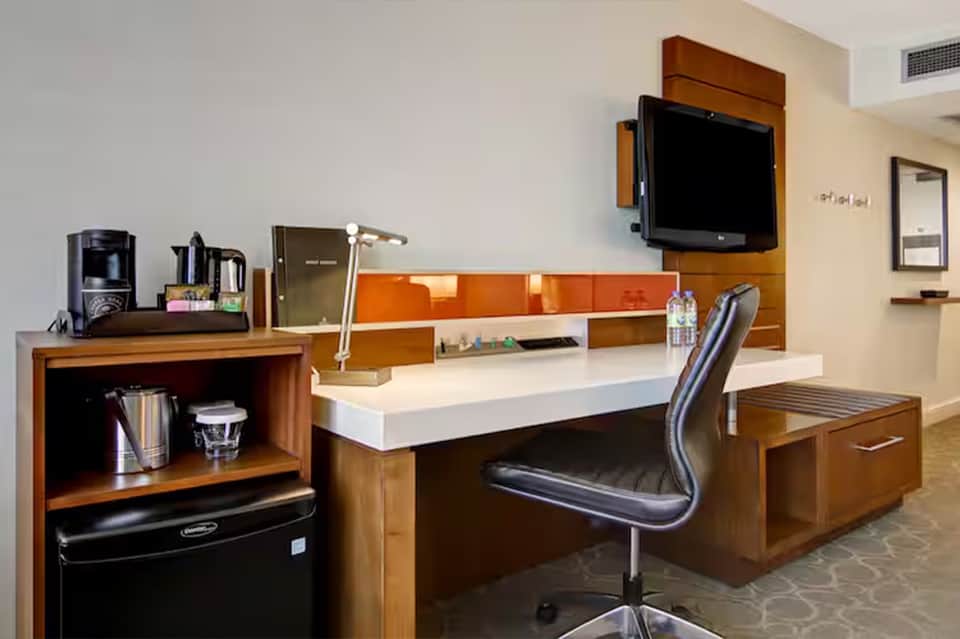 Hotel room workspace with desk, TV, wooden furniture, and orange accent wall