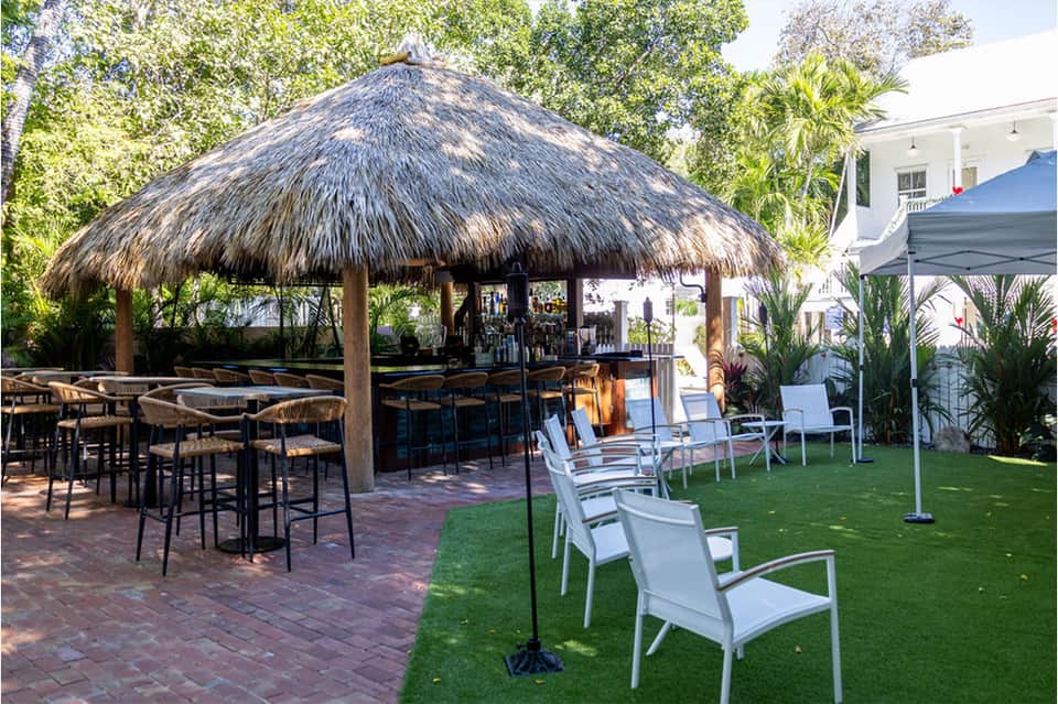 Tiki bar with thatched roof, high-top seating, lawn chairs, and green space at tropical resort property