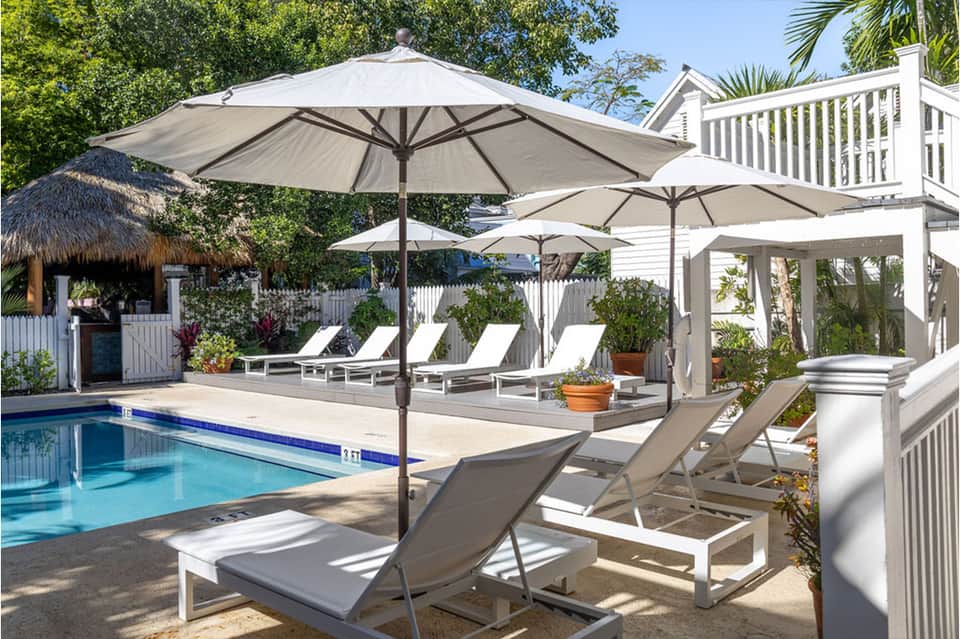 Resort pool with thatched cabana, white lounge chairs under large umbrellas, and charming coastal architecture.
