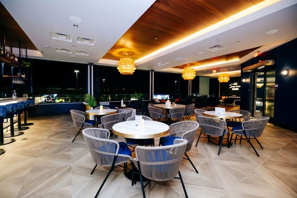 Elegant rooftop dining area with round tables, modern chairs, pendant lighting, and night views