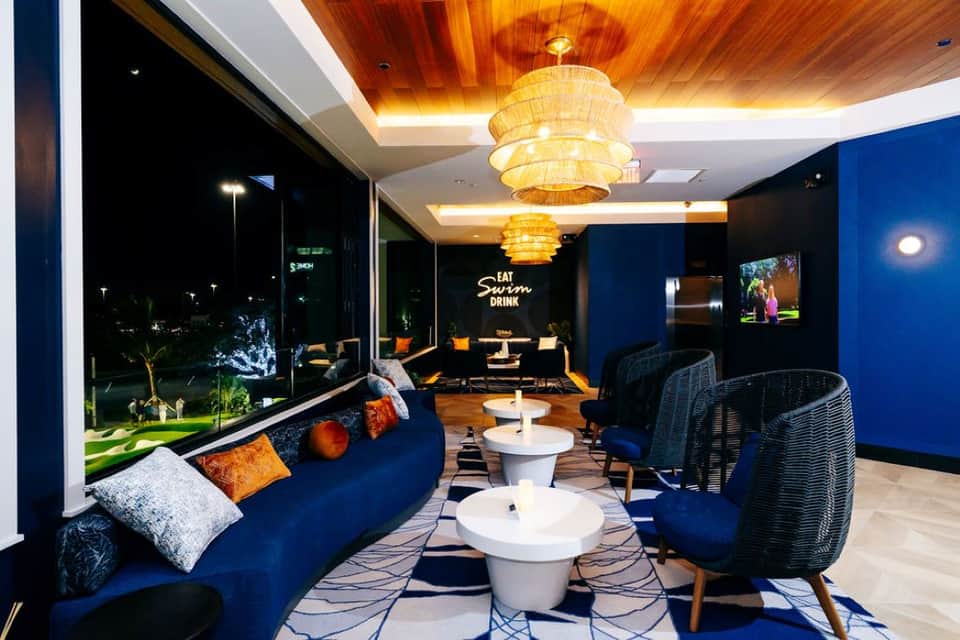 Modern lounge with blue seating, woven pendant lights, and views of grounds at night