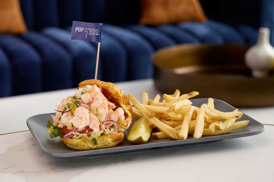 Gourmet shrimp sandwich with fries served at Pop Stroke restaurant with blue velvet seating in background