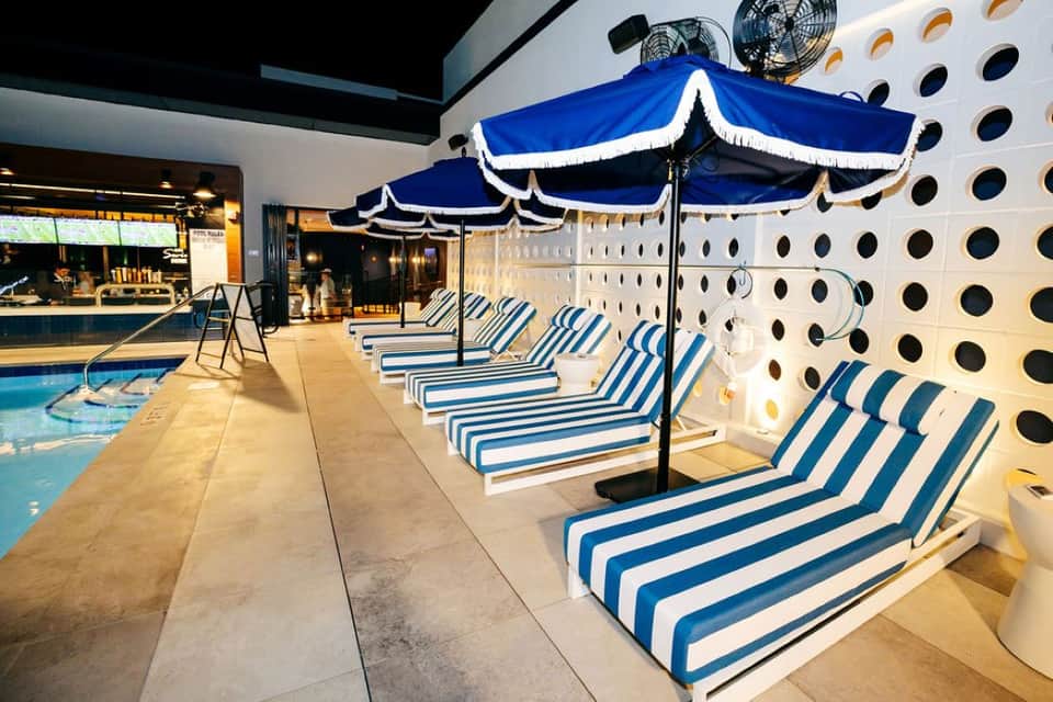 Indoor pool area with blue and white striped loungers under matching umbrellas, white perforated wall backdrop