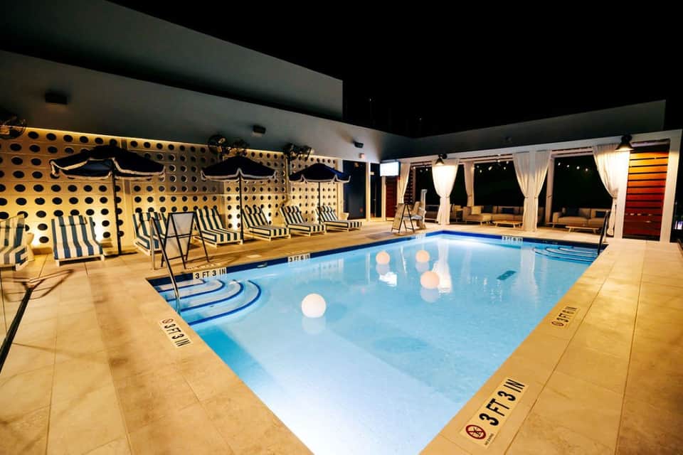 Indoor swimming pool at night with striped lounge chairs and illuminated perforated wall backdrop