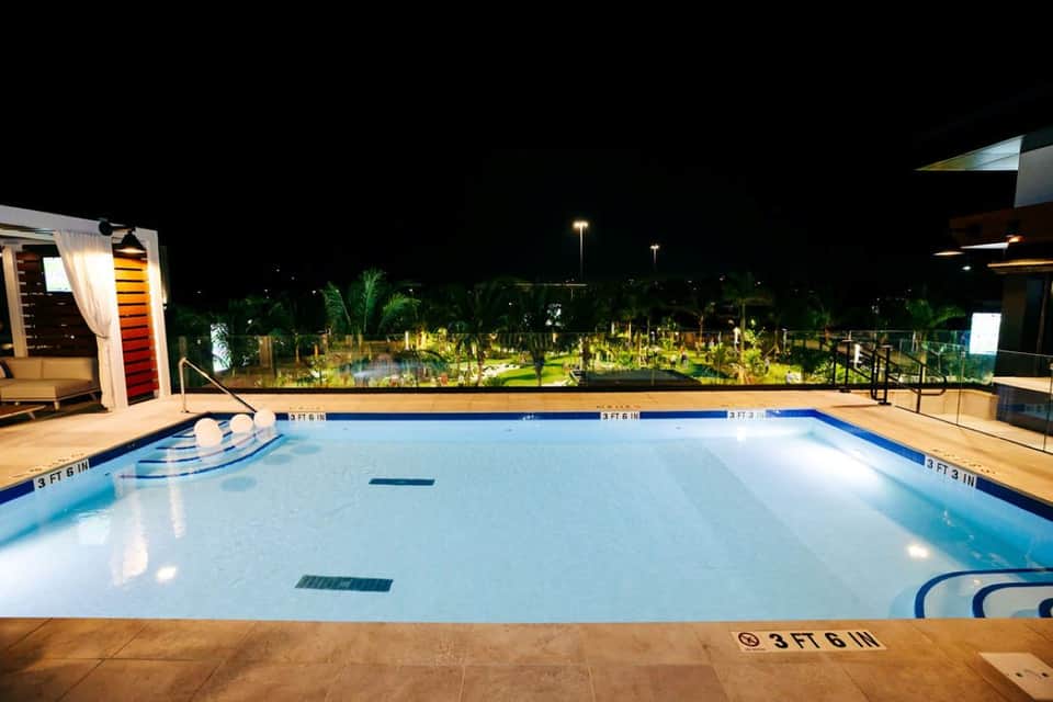 Empty resort swimming pool at night with lit landscaping and palm trees