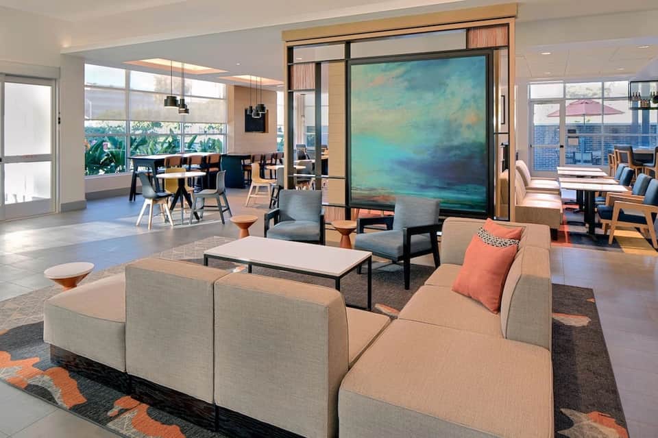 Modern hotel lobby lounge with modular beige seating, abstract ocean artwork, and floor-to-ceiling windows