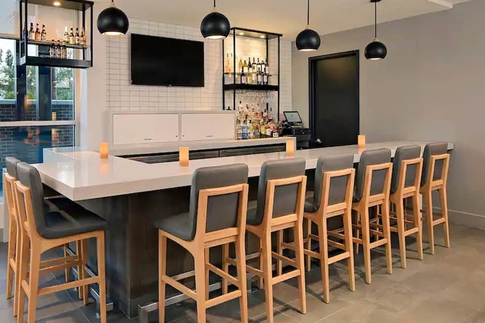 Modern bar counter with light wood stools, black pendant lights, and stocked shelving behind