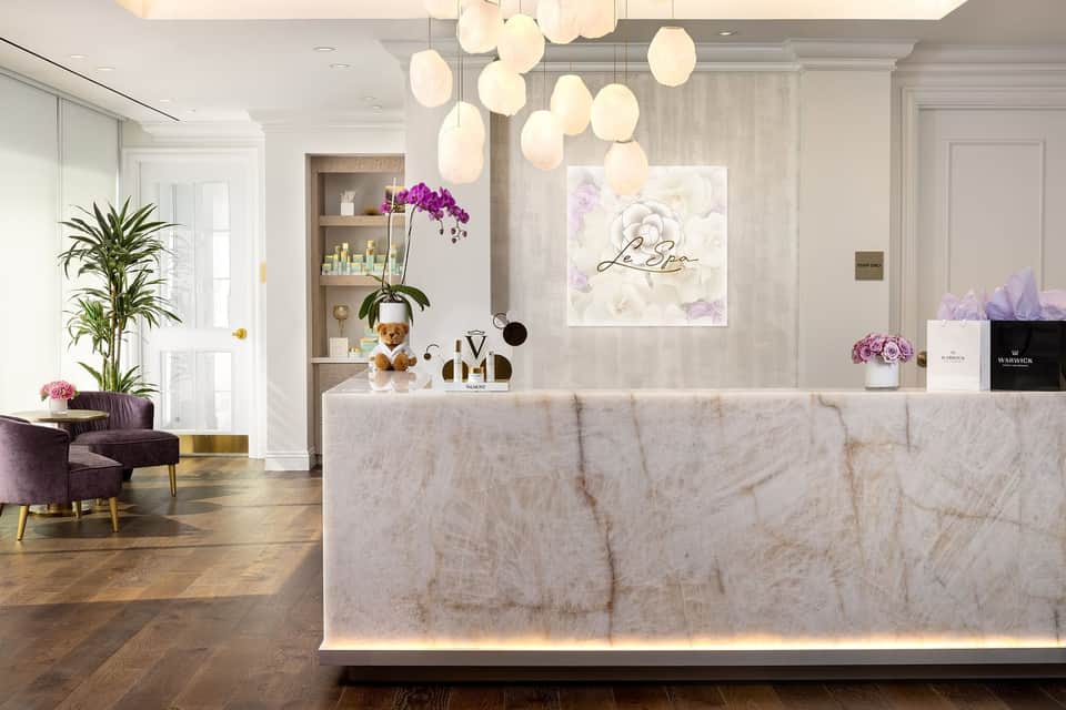 Luxury hotel lobby with marble reception desk, pendant lighting, and floral arrangements