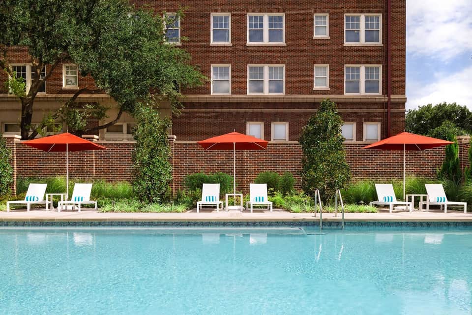 Resort pool surrounded by red umbrellas, white lounge chairs, ivy-covered brick building, and manicured landscaping