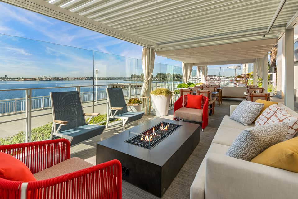 Waterfront terrace with lounge seating, fireplace, red accent chairs, and bay views