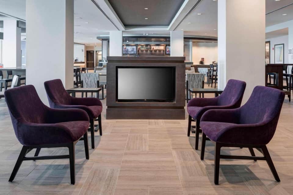 Modern hotel lounge with purple accent chairs, fireplace, and flat-screen television