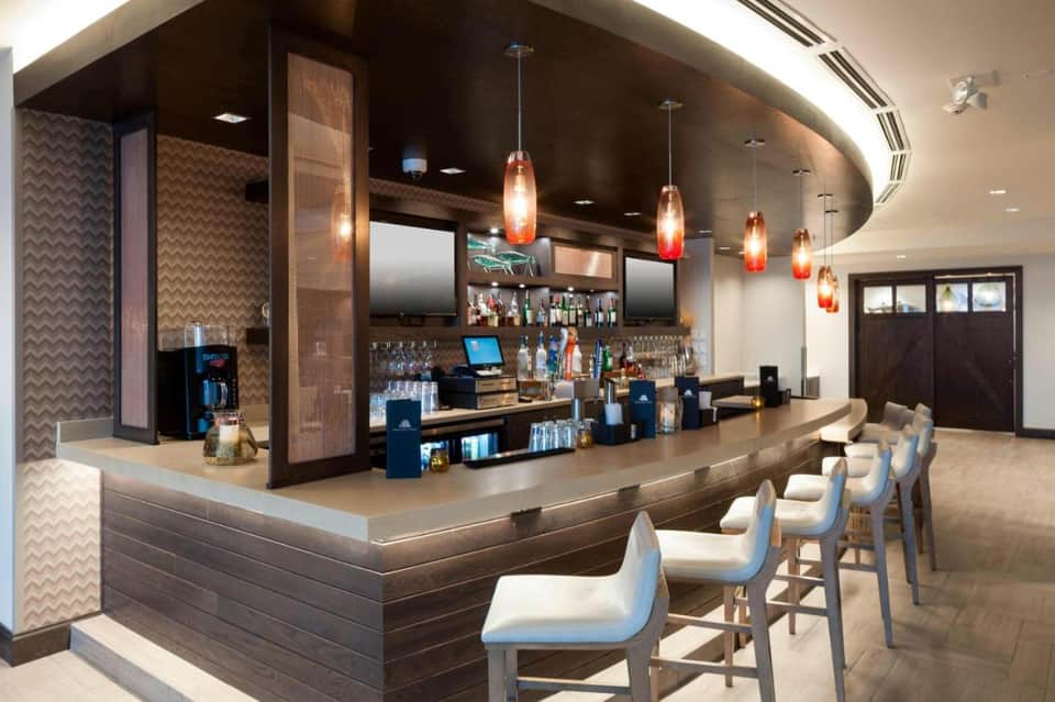Modern hotel bar with curved counter, pendant lights, wood accents, and bar seating
