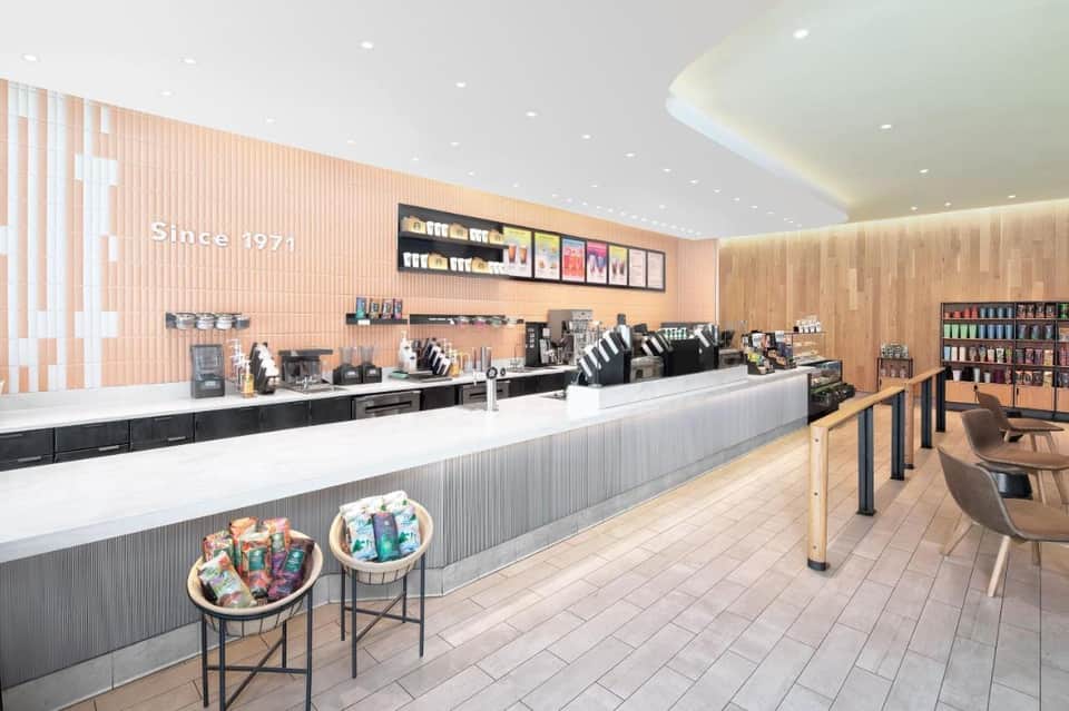 Contemporary coffee shop interior with light wood accents, white counter, peach-colored wall panels, and since 1971 signage