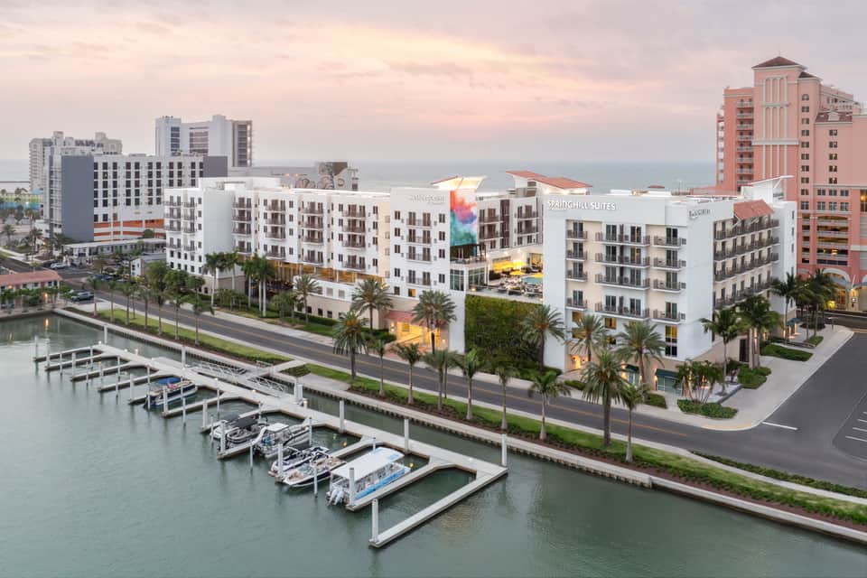 Waterfront resort complex with white buildings, palm trees, and moored boats along canal
