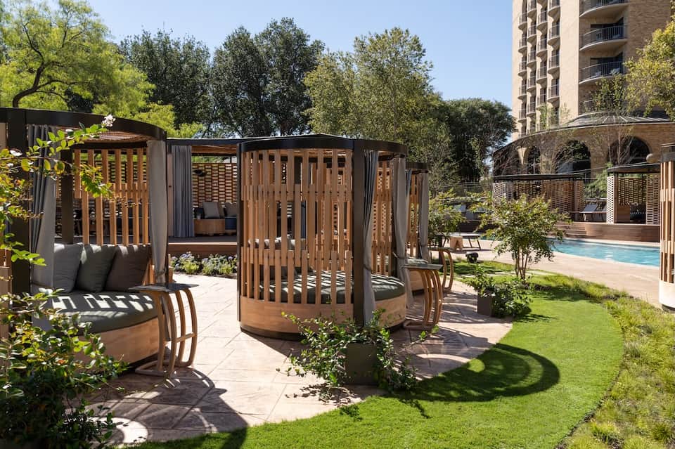 Wooden cabanas and seating areas with lounge chairs near resort pool and building