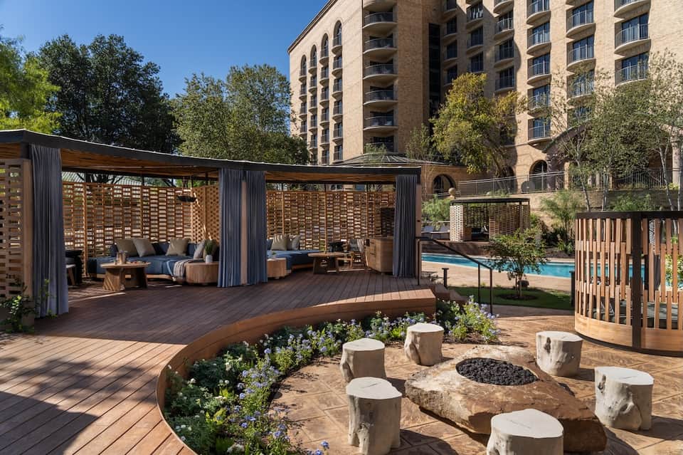 Hotel courtyard with wooden pergolas, lounge seating, pool area, and residential building backdrop