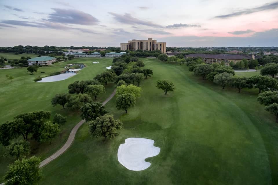 Aerial view of resort on golf course with fairway bunker, trees, pond, and main building in distance