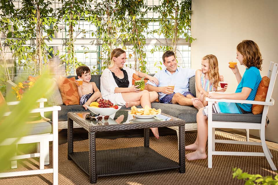 Family relaxing in modern conservatory with lush green plants, comfortable seating, and natural light