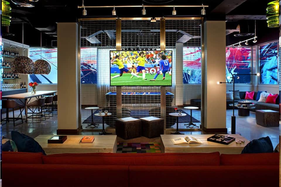 Sports bar lounge with large TV screen showing soccer match, red sofa, and modern lighting