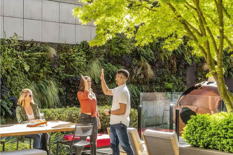 Outdoor patio with guests socializing among lush green vegetation and modern architecture