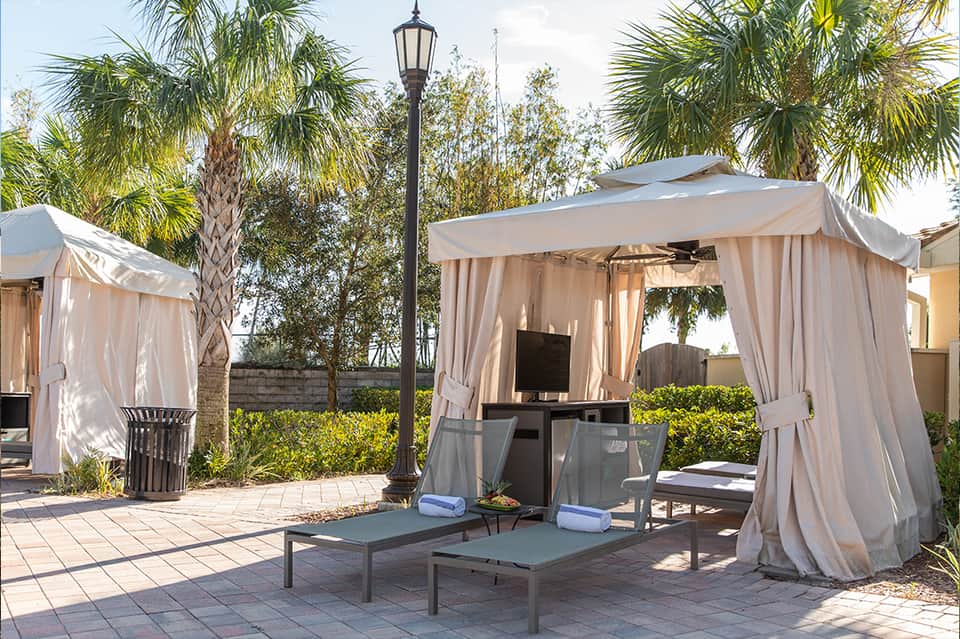 Outdoor cabanas with flowing white curtains, lounge chairs, and palm trees on resort patio