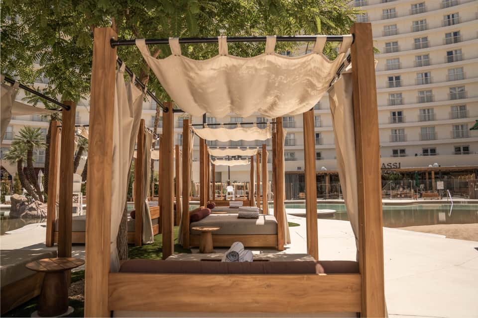 Wooden canopy beds with cream drapes overlooking pool and urban skyline