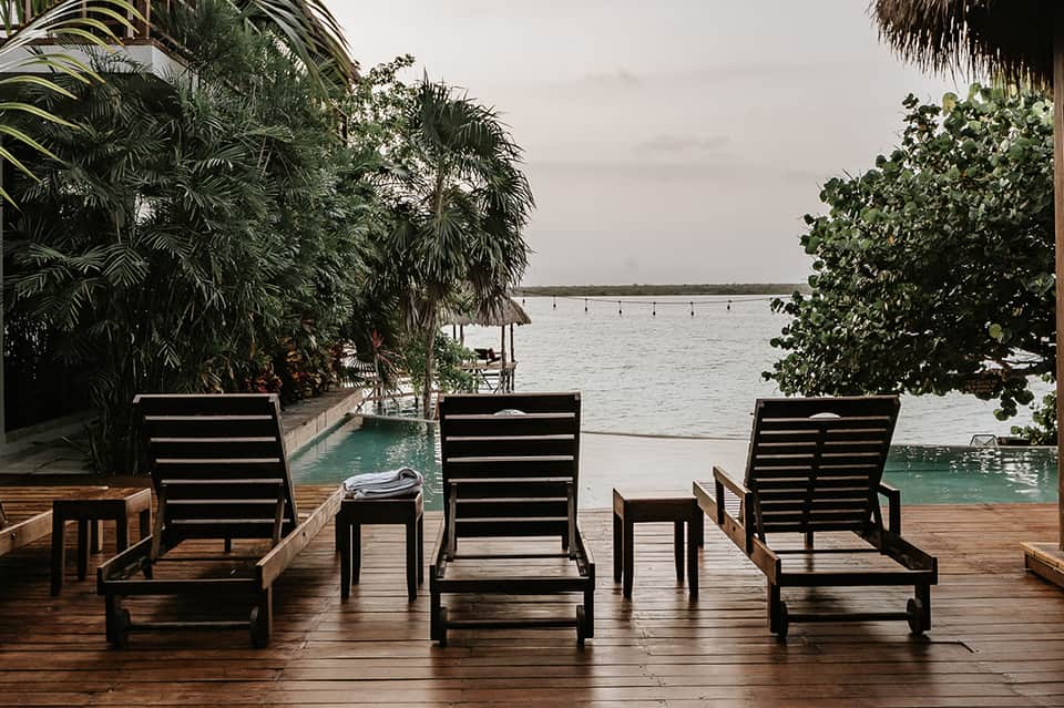 Waterfront lounge chairs on wooden deck overlooking bay with palm vegetation
